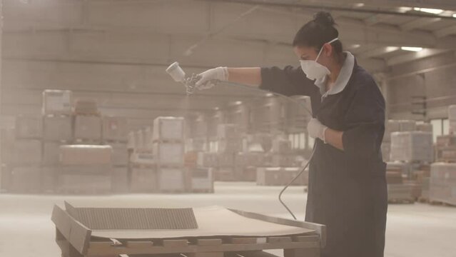 Woman with Mask Spray Painting Ceramic Tiles in a Factory, Extreme Slow Motion