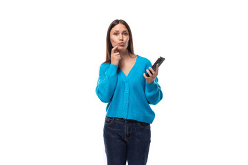beautiful cute young woman dressed in a blue cardigan thinks holding a phone in her hand