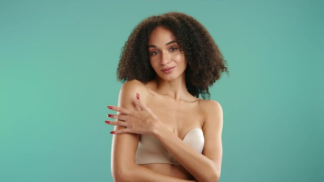 Cute curly-haired sexual lady in strapless bra with mouth slightly open seductively running her fingers on shoulder and neck isolated on green background. High quality 4k footage