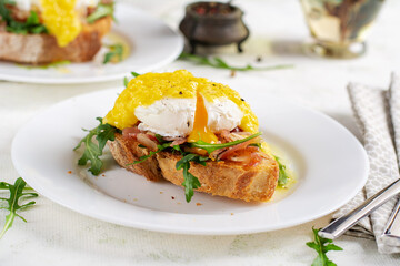 Breakfast. Sandwich with ham, poached egg, onion and arugula in a plate on a light background