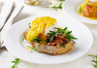 Breakfast. Sandwich with ham, poached egg, onion and arugula in a plate on a light background