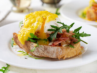 Breakfast. Sandwich with ham, poached egg, onion and arugula in a plate on a light background
