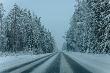 Fototapeta premium A Wintry Path Through a Chilly Forest with Snow Covered Trees. Winter road through snowy forest, tree lined and cold temperature.