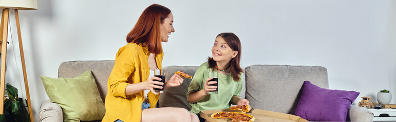 cheerful mother and teenage daughter with pizza and soda on cozy couch in living room, banner
