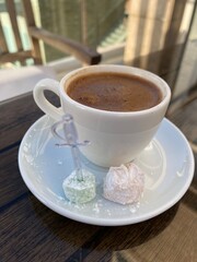 closup of a cup of turkish cofee shwoing foam on top with turkish delight on the side.