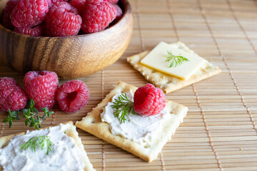 Vegan cream cheese on top of a salty cracker with raspberries and fresh herbs. Vegan food concept.