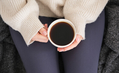 Top view of young woman's hands in white sweater holding her morning coffee.Peaceful times at home