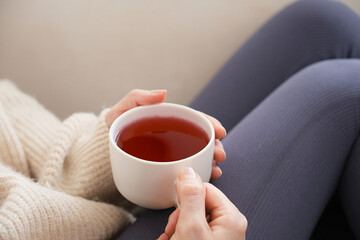 Side view young woman holding a white cup herbal tea.
Young woman sitting on a white sofa pampering...