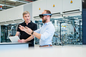 Technician wearing augmented reality glasses in a factory interacting with colleague