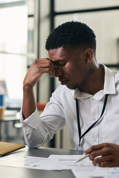 Tired young businessman sitting with documents in office
