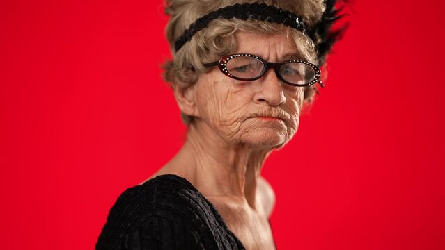 Closeup funny portrait of elderly old woman toothless, giving heart gesture with hands isolated on red background wearing wig, glasses