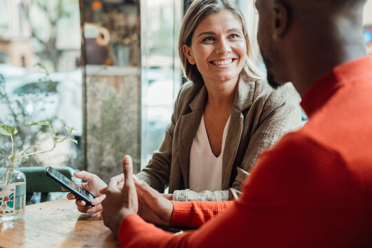 Happy businesswoman looking at colleague sitting in cafe