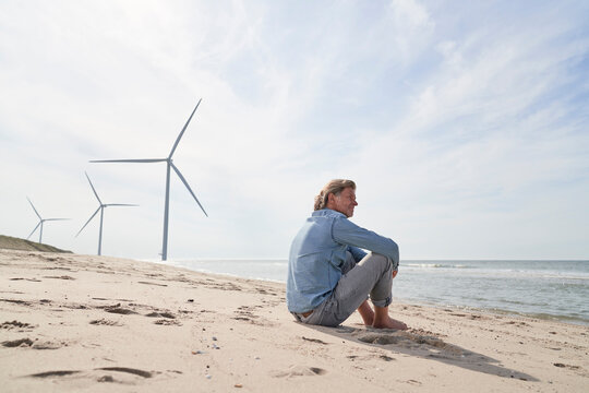 Senior businessman sitting in front of wind turbines at beach