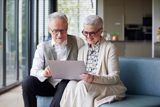 Senior couple sitting on couch at home using tablet PC
