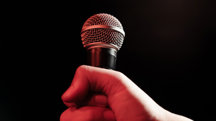 A man's hand holds a professional microphone against the background of stage light.