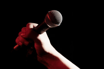 A man's hand holds a professional microphone on a black background.