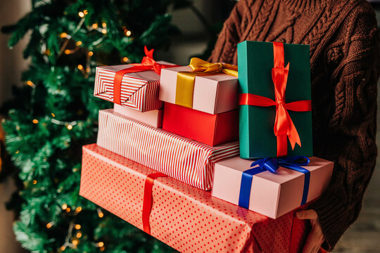 Woman holding presents near Christmas tree at home