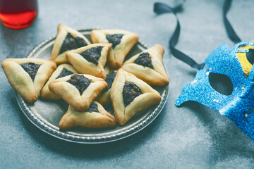 Traditional Hamantashen triangular cookie with poppy seed filling, wine, carnival masks on a concrete background. top view. Purim celebration concept. Jewish carnival holiday