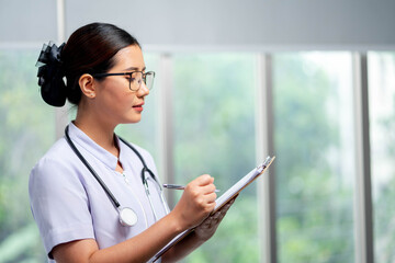 Asian Young female nurse is looking at the patient medical record after pay a ward visit for better...