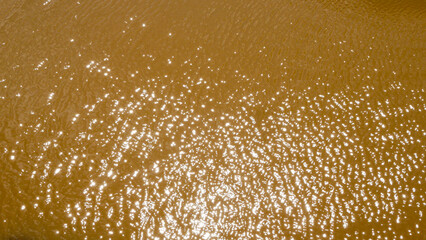 Aerial view of murky and dirty brown river water with reflections of sunlight shining through the...