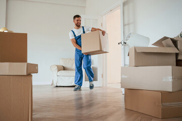 White shirt and blue uniform. With box in hands. Moving service employee in a room