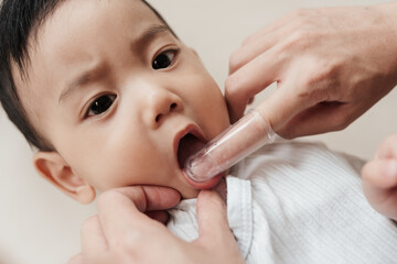Cleaning Asian baby's mouth by brushing his teeth. Baby care, baby's first teeth. Closeup Shot,...