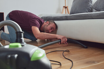 Fototapeta na wymiar Man cleaning apartment with vacuum cleaner.