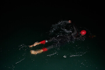 A determined professional triathlete undergoes rigorous night time training in cold waters,...