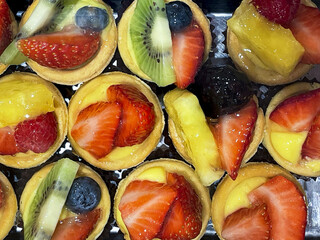 row of tarts filled with seasonal fruit seen from above in a pastry shop counter