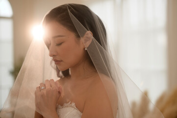 Beautiful bride in wedding dress covered by white veil, folding her arms and praying on ceremony, Love and marriage concept