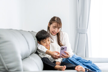 Fototapeta premium ソファでスマホの画面を見る母親と男の子