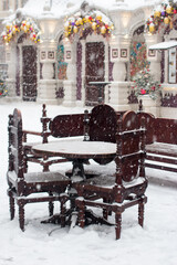 A wooden table with chairs are standing outside under the snow. Cafe tables on the outdoor veranda in winter