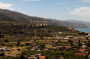 Scenic landscape view of Sicily at sunny day. Curved automobile viaduct in mountains near Santo Stefano di Camastra. Small houses near the sea. Travel and tourism concept. Sicily, Italy