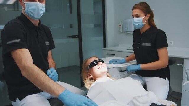 Young woman client lying in dentist chair of modern office clinic. Dental practitioner with assistant start medical teeth treatment and correction. Medication. Healthcare.