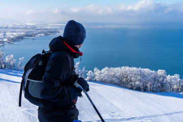Person in snowcovered landscape on a mountain looking down onto a deep blue lake - obrazy, fototapety, plakaty