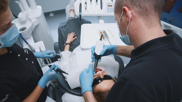 Caucasian woman visiting private clinic dental care office for teeth correction. Couple of dentists doing check-up of patient oral cavity for treatment or surgery. Closeup shot.
