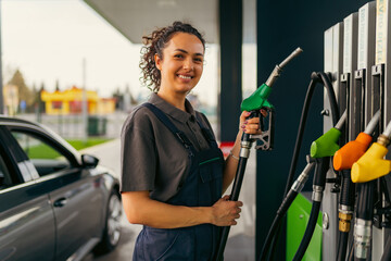 A young woman works at a gas station, holding a fuel hose