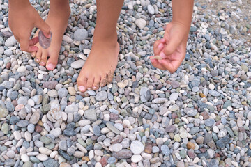 Child's feet and hands engage with a myriad of stones, illustrating active discovery.