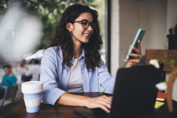 Smiling woman sitting with smartphone and laptop at table