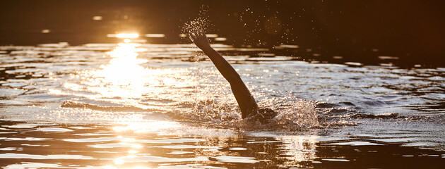 Triathlon athlete swimming on lake in sunrise wearing wetsuit