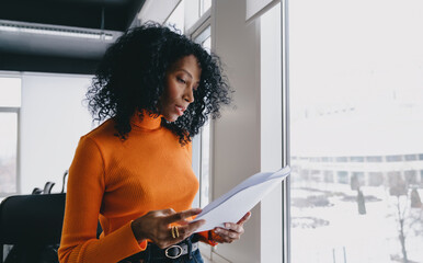A perceptive analyst in a bold orange sweater scrutinizes financial reports in a bright office