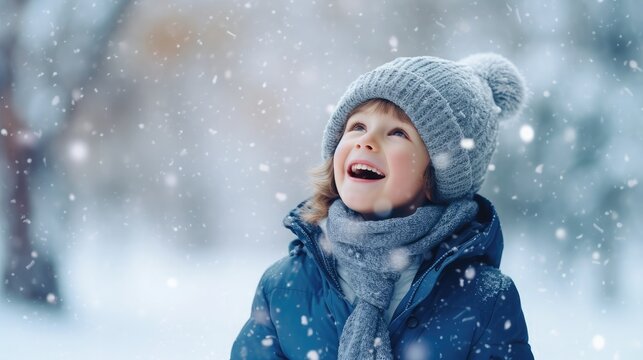 Funny excited little boy in blue winter clothes walks during a snowfall. Outdoors winter activities for kids. Cute child wearing a warm hat catching snowflakes with his tongue