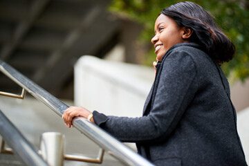 Young Black career woman walking up stairs outside while talking on the phone