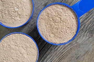 Three supplement scoops in formation close up filled with protein powder on top of wooden kitchen surface. Dietary supplements concept – flat lay, top view.