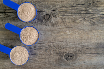 Three supplement scoops in a row filled with protein powder on top of wooden kitchen surface....