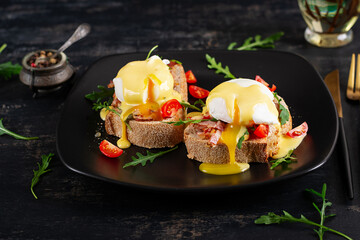 Breakfast. Sandwich with ham, poached egg, onion and arugula in a plate on a dark background