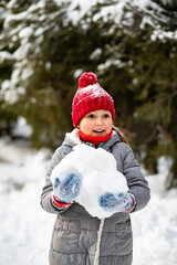 Cute little girl in winter sunny day standing near by spruce outdoor and holding big snowball for making snowman. Outdoor winter activity. Happy childhood. Christmas and New Year concept.