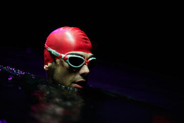 A determined professional triathlete undergoes rigorous night time training in cold waters, showcasing dedication and resilience in preparation for an upcoming triathlon swim competition - obrazy, fototapety, plakaty