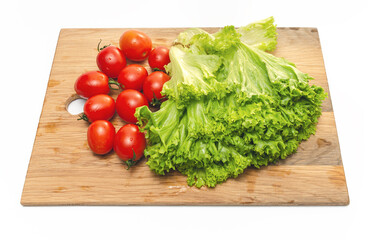 Bright red cherry tomatoes and green lettuce on a wooden board. Vegan food. Salad preparation.