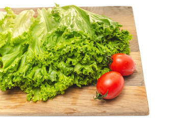 Two red cherry tomatoes and green lettuce on a wooden board. Vegan food. Salad preparation.